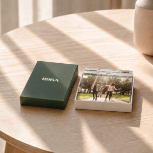 Caixa de fotos verde Kora aberta, com fotografias impressas de momentos entre amigos.