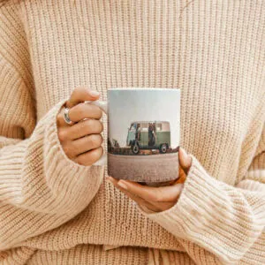 Pessoa a segurar uma caneca personalizada com fotografia de uma carrinha, vestindo uma camisola de malha bege.