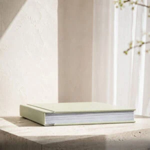 Álbum de fotografias premium fechado com capa verde-clara e páginas espessas.